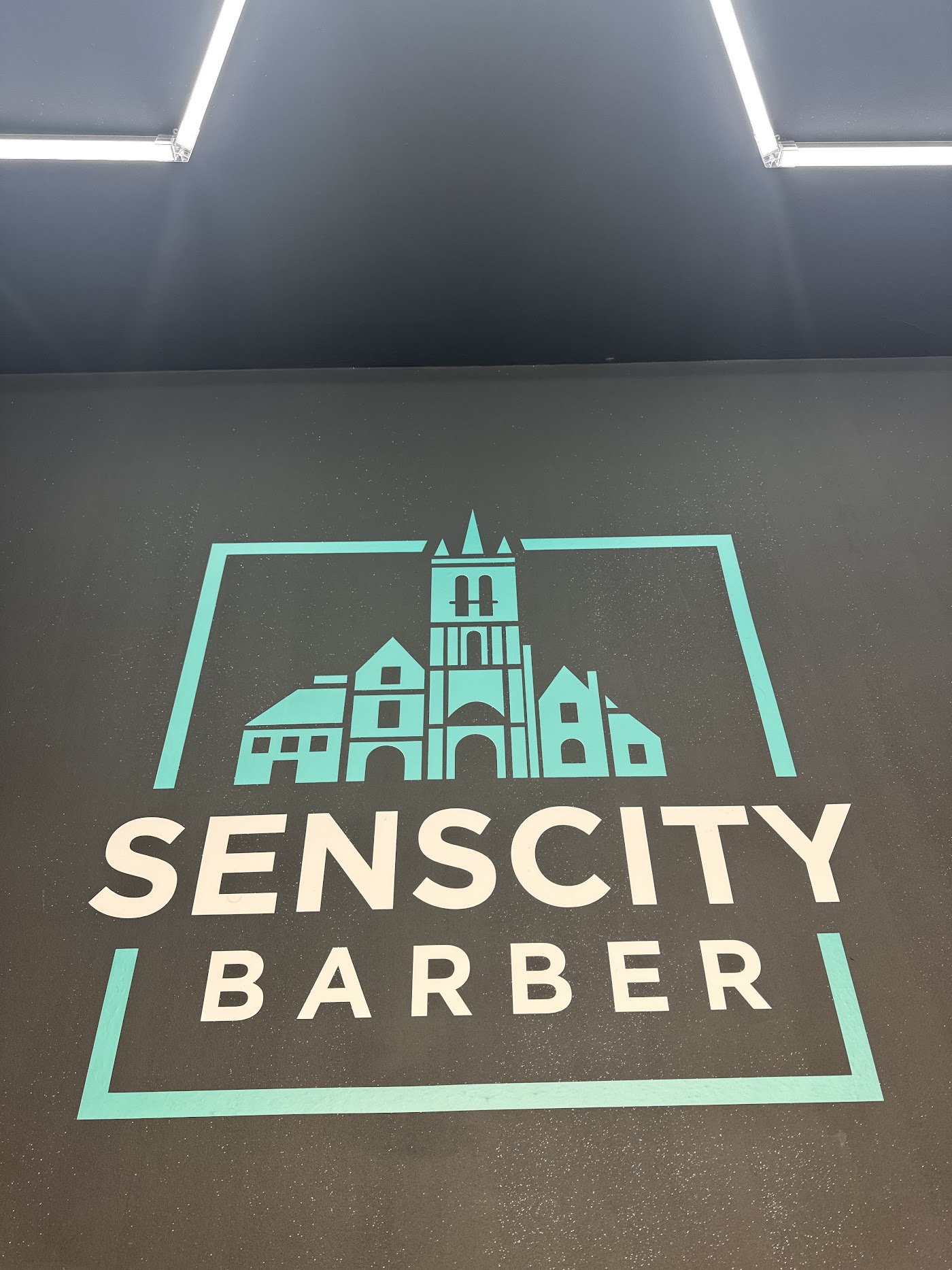 Le logo Sens City Barber peint sur le mur du salon